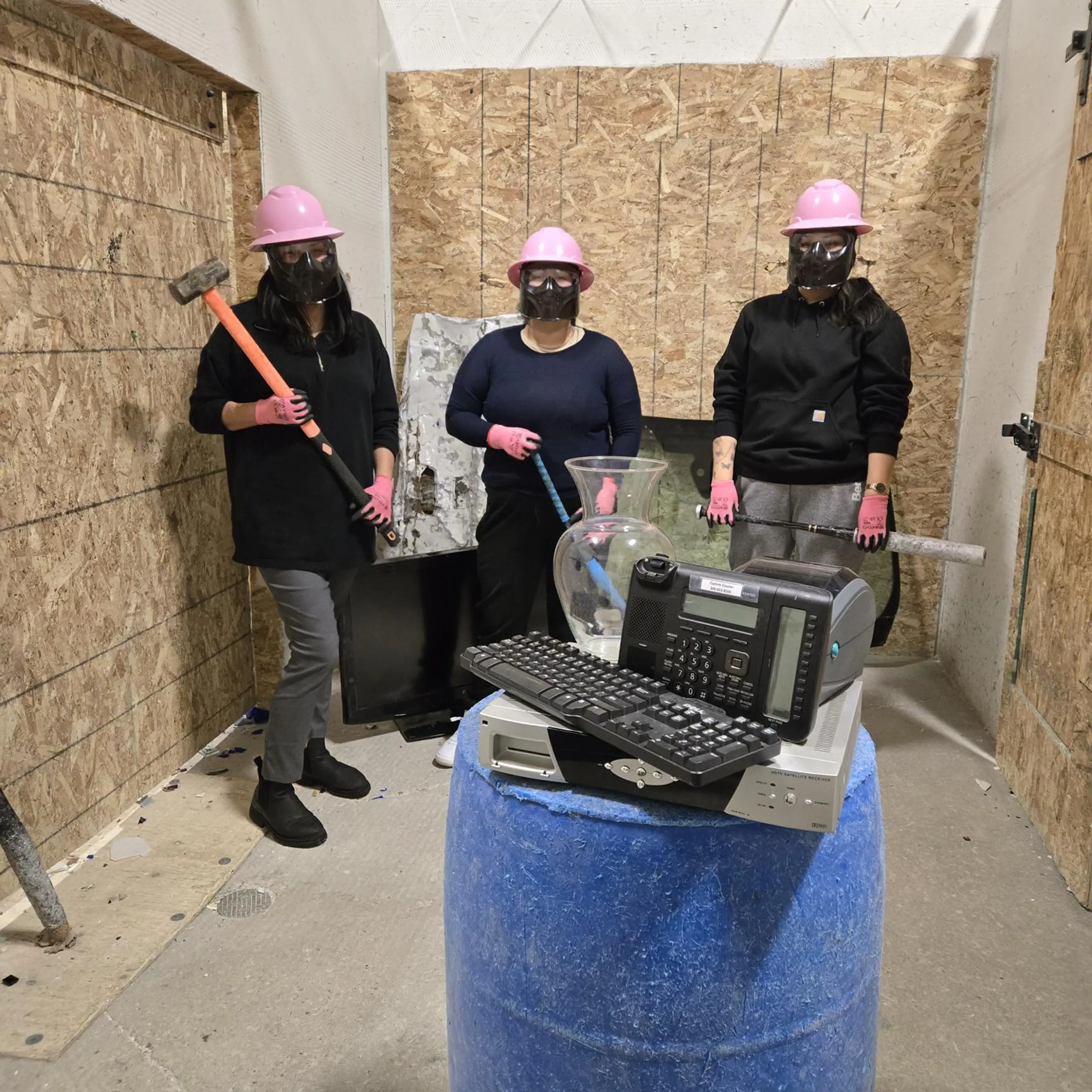 Group of people wearing protective gear holding hammers and bats ready to smash a pile of electronics